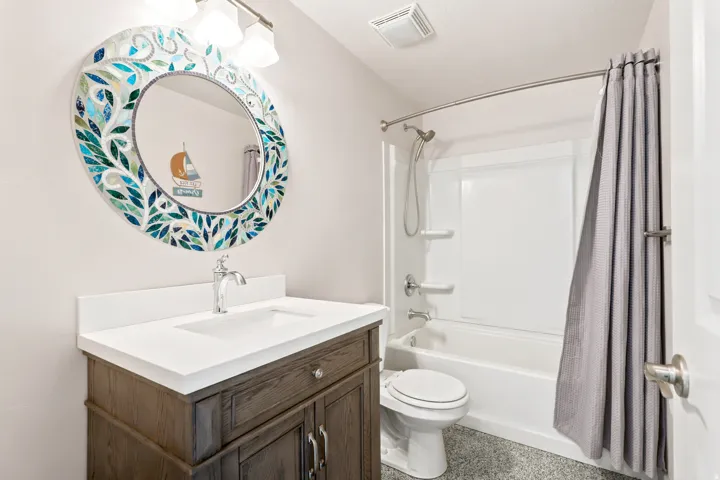 Wood-finish vanity with a white countertop and integrated sink, chrome faucet, and decorative mosaic mirror