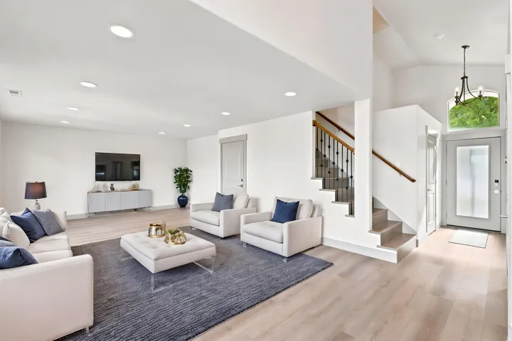 Open-concept living area with wood-finish flooring, recessed lighting, and a staircase featuring a wooden handrail and wrought iron balusters