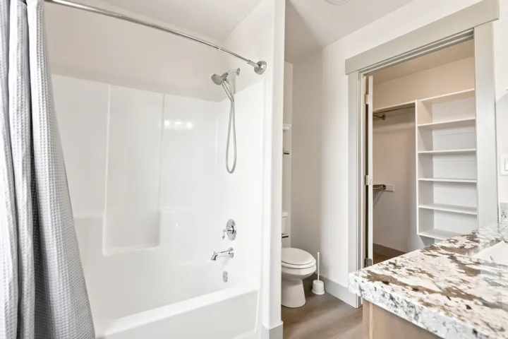 White tub and shower combination with chrome fixtures, granite-finish countertop, and built-in closet shelving