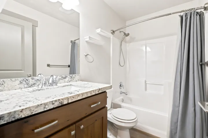 Bathroom featuring a wood vanity with a stone countertop, an undermount sink, a chrome faucet, a shower-tub combination with a wall-mounted shower head, and a toilet