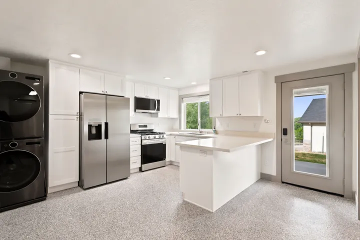 White shaker cabinetry, stainless steel appliances, white countertops, built-in shelving, and a glass-paneled exterior door