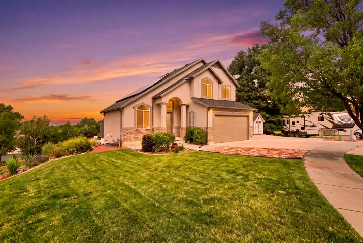 Stucco exterior with stone accents, arched entry, two-car garage, solar panels, and a concrete driveway