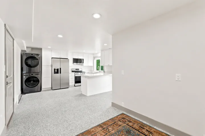 White shaker cabinetry, stainless steel appliances, white island, recessed lighting, and a stackable washer and dryer