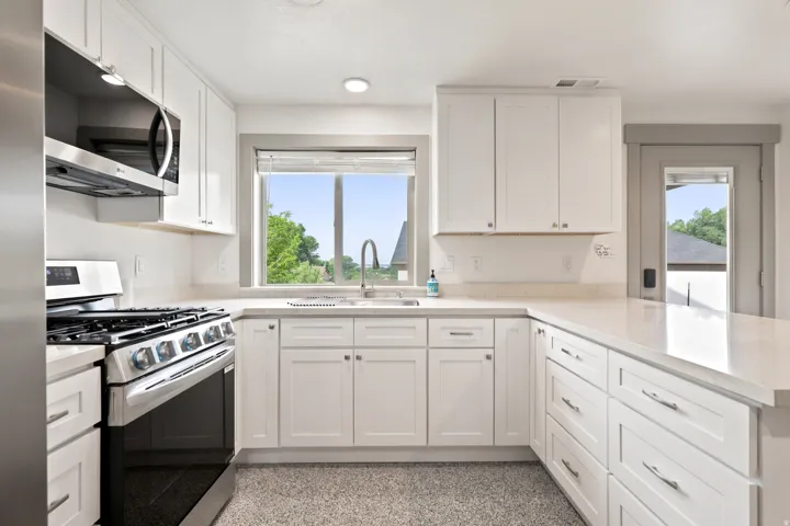 White cabinetry with chrome hardware, an integrated stainless steel microwave, a stainless steel range, light-toned countertops, and a single basin sink with a gooseneck faucet
