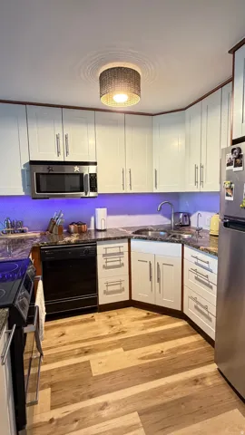 Kitchen featuring wood-finish flooring, white cabinetry with modern hardware, dark stone-finish countertops, stainless steel appliances, and a built-in microwave