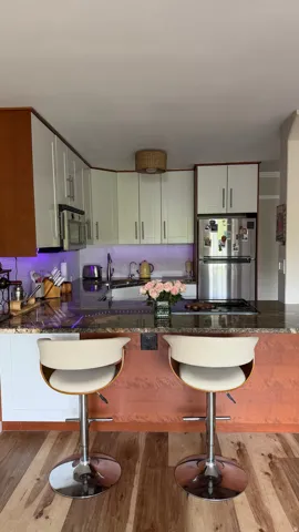 Kitchen featuring wood-finish flooring, white cabinetry, integrated stainless steel appliances, and a polished stone countertop