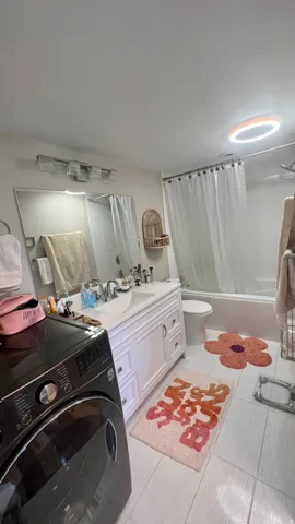White tile flooring, white vanity with integrated sink, chrome fixtures, tub with shower, and built-in laundry appliances
