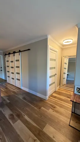 Wood-finish flooring, crown molding, modern light fixture, and contemporary doors with frosted glass panels