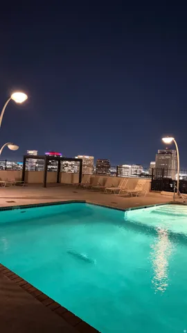 Rooftop pool with illuminated waters, surrounded by concrete decking and a metal privacy fence