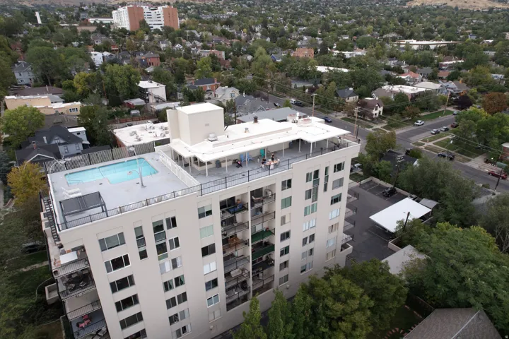 High-rise building with a rooftop swimming pool, expansive rooftop deck, multiple private balconies, and an adjacent parking area