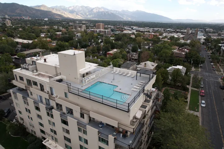 Rooftop pool and spa deck with resort-style amenities, featuring a sparkling blue swimming pool, sun lounging areas, and panoramic mountain backdrop