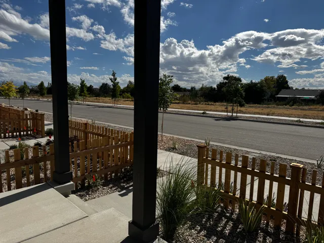 Concrete walkway, wood picket fence, low-maintenance landscaping, wide street, and established trees