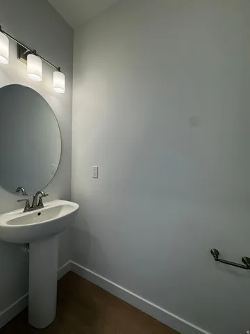 Pedestal sink with a brushed nickel faucet, round wall mirror, and a three-light vanity fixture