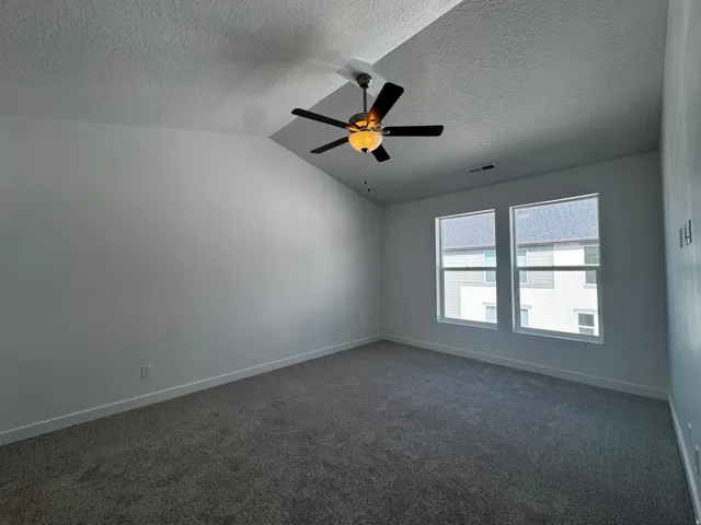 Vaulted ceiling featuring a ceiling fan with integrated lighting, dual windows, and textured carpeting