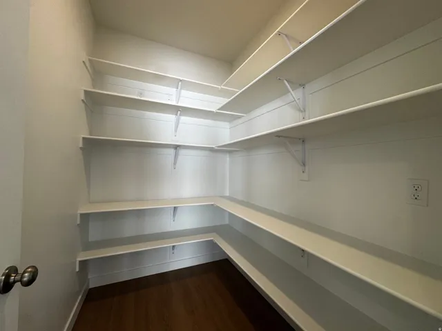 Spacious walk-in pantry with extensive built-in shelving, durable wood-finish flooring, and electrical outlets
