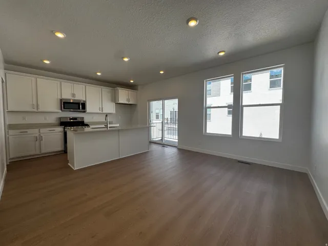 Kitchen featuring white cabinetry, stainless steel appliances, a center island with sink, and wood-finish flooring