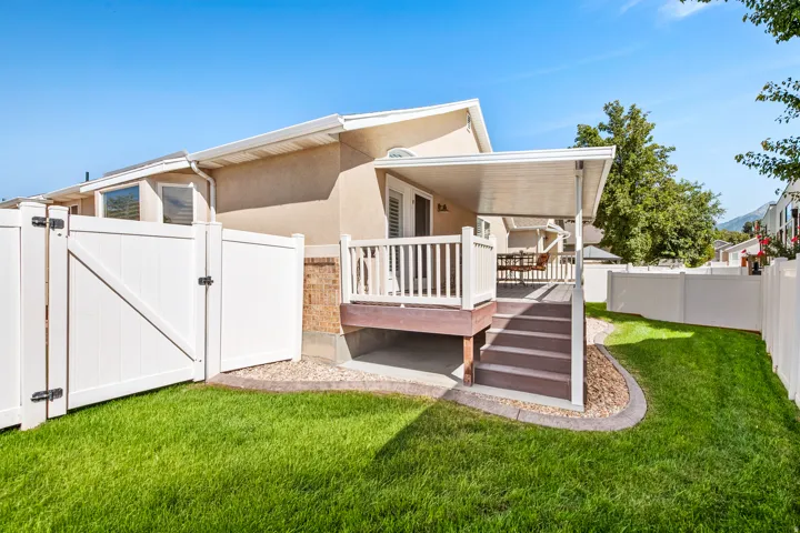Expansive manicured lawn area with white privacy fencing, covered patio, outdoor deck with railings, and exterior brick accents.
