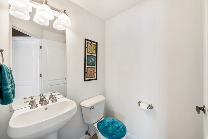 Half bath on main level w/pedestal sink & toilet w/brushed nickel fixtures, wall-mounted mirror, and vanity lighting with decorative glass shades.