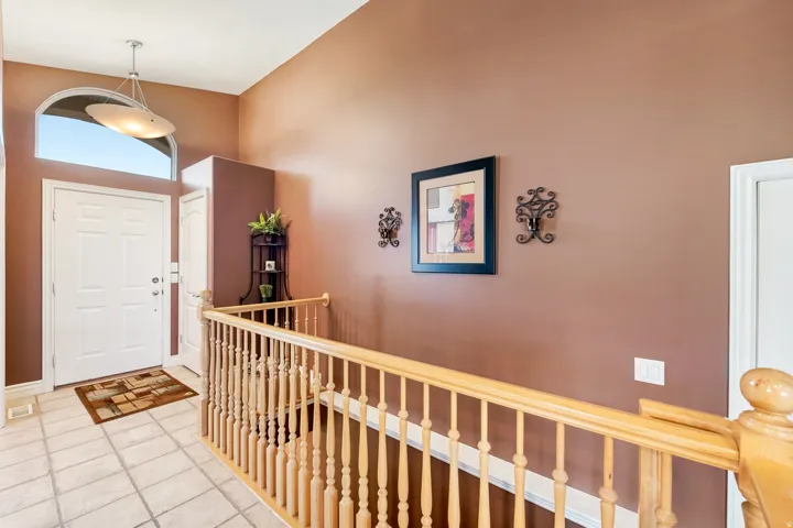 Entryway featuring an arched transom window, tiled flooring, wood-finish railing, and a contemporary pendant light fixture.