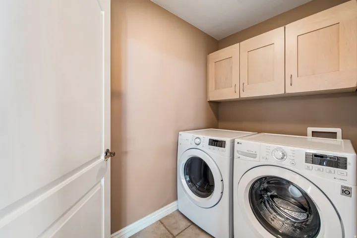 Integrated laundry area on main level, featuring light wood cabinetry & tile flooring.