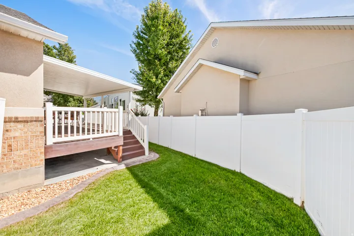 Spacious backyard featuring a manicured lawn, mature landscaping, and white vinyl privacy fencing