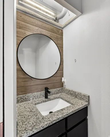 Vanity with an integrated sink, granite countertop, matte black faucet, and wood-finish accent wall