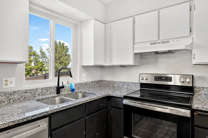 Stainless steel dual basin sink with a matte black high-arc faucet, granite-patterned countertops, and upper white cabinetry