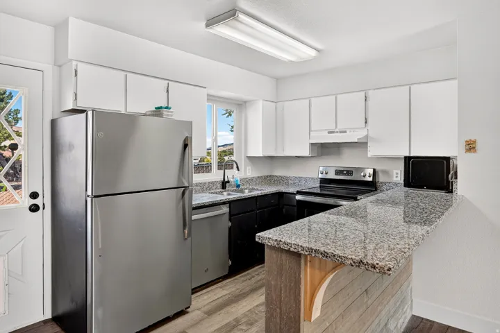 Kitchen featuring stainless steel appliances, granite countertops, white cabinetry, wood-finish flooring, and a breakfast bar
