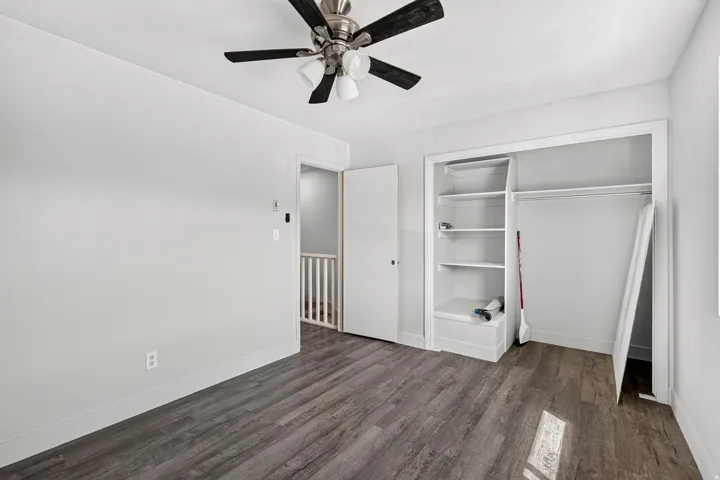 Wood-finish flooring, overhead ceiling fan with lighting, built-in shelving, and closet rod