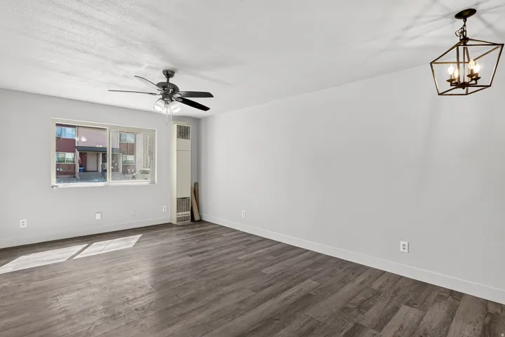 Spacious room featuring wood-finish flooring, a contemporary ceiling fan, and an overhead geometric light fixture