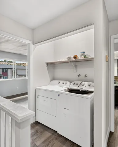 Dedicated laundry area with a built-in shelf, clothing rod, and wood-finish flooring
