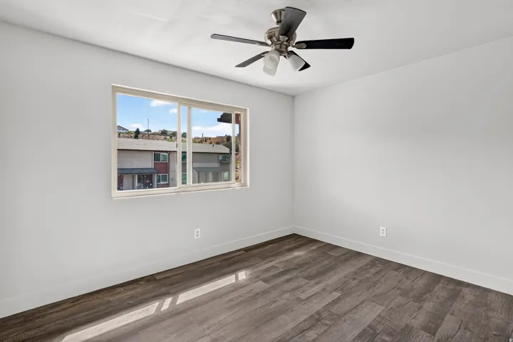 Wood-finish flooring, ceiling fan with integrated lighting, and a window with white trim