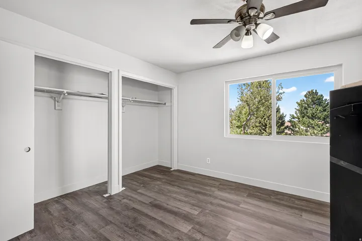 Room featuring wood-finish flooring, a ceiling fan, a window, and dual closets with hanging rods