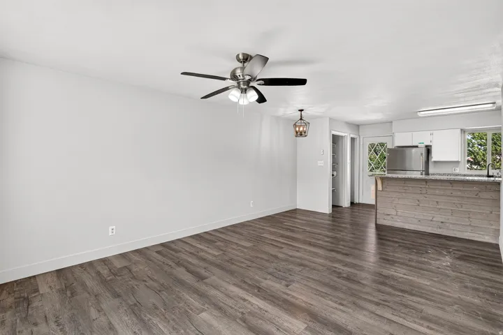 Wood-finish flooring, ceiling fan, contemporary pendant lighting, kitchen island with shiplap-style paneling, and a stainless steel refrigerator