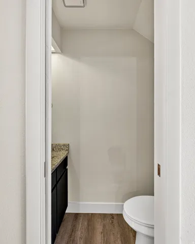 Powder room featuring a dark wood-finish vanity, light-toned countertop, wood-finish flooring, and a white toilet