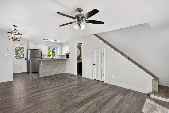 Wood-finish flooring, ceiling fan with integrated lighting, built-in kitchen cabinetry with stainless steel appliances, kitchen island with wood-paneled facade, and a carpeted staircase