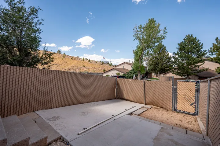 Concrete patio space, chain-link fencing with privacy slats, metal gate, graded landscaping, mature trees