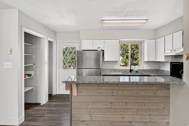Kitchen featuring white cabinetry, gray stone countertops, a stainless steel refrigerator, and wood-finish flooring