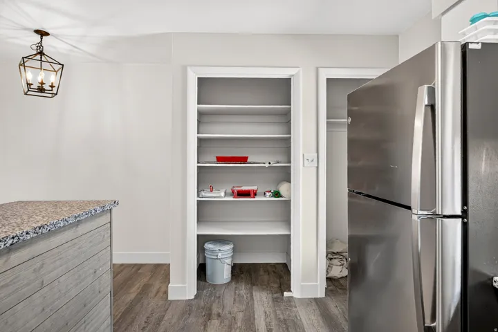 Wood-finish flooring, built-in shelving, stainless steel refrigerator, and a stone-look countertop