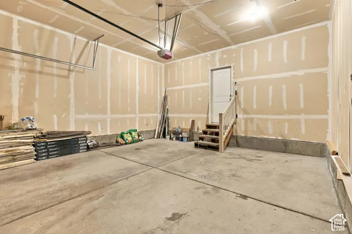 Concrete flooring, built-in staircase with wood handrail, interior access door, overhead lighting, and an automatic garage door opener