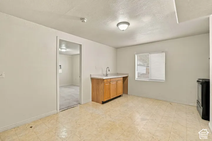 Tile flooring, wood-finish cabinetry, countertop with integrated sink, window with blinds, and ceiling-mounted light fixture