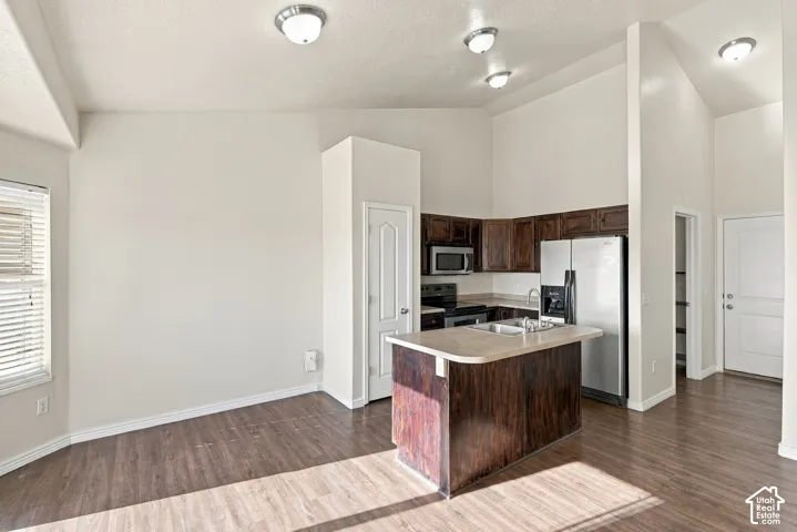 Vaulted ceilings above the kitchen with wood-finish flooring, dark wood cabinetry, and a kitchen island with a built-in sink