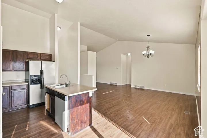 Open-concept living space featuring wood-finish flooring, vaulted ceilings, and a kitchen island with integrated sink