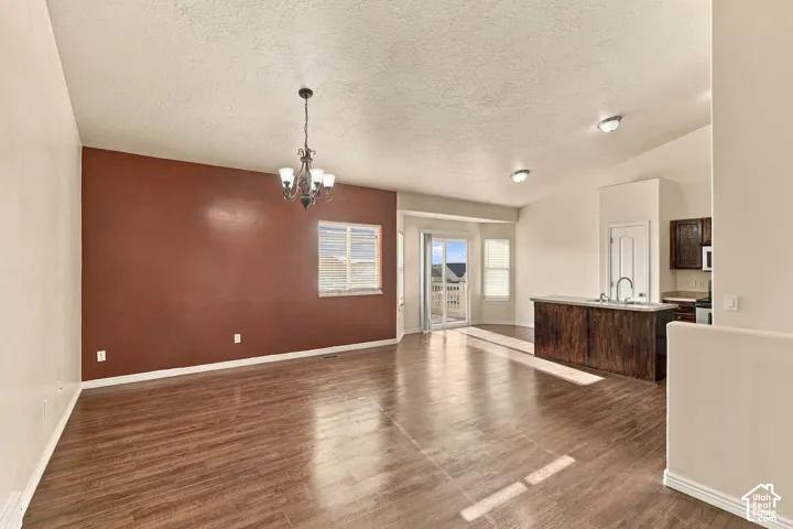 Vaulted ceilings, wood-finish flooring, a contemporary chandelier, and sliding glass door access to an exterior deck