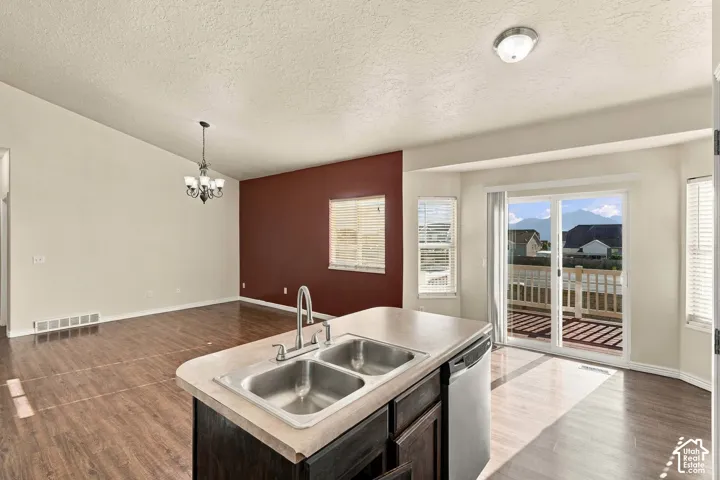 Kitchen island with double basin stainless steel sink, wood-finish flooring, sliding glass door access to an exterior deck, and a dining area with a chandelier