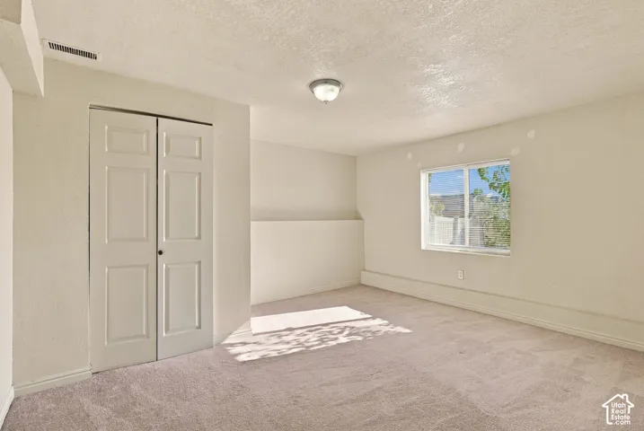 Carpeted flooring, window with white trim, built-in bi-fold closet doors, wall-mounted light fixture
