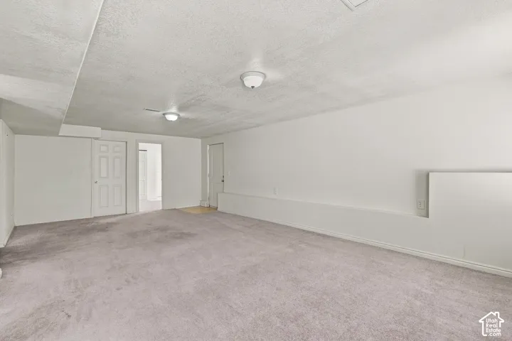 Expansive carpeted area with white walls and ceiling, featuring two flush-mount light fixtures