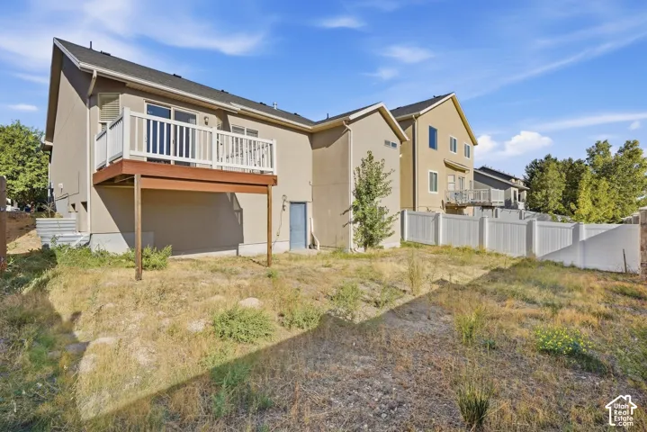 Exterior featuring a neutral stucco finish, attached deck with white railing, sliding glass door access, and a sloped terrain