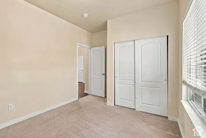 Sliding closet doors with arched paneling, carpeted flooring, and a large window with horizontal blinds