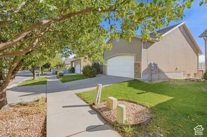 Stucco exterior with a two-car garage, concrete driveway, and landscaped front yard with mature trees